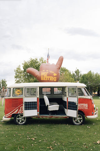 Mo' Bettahs VW Bus, with side doors open showing inside. There's a large inflatable 'Hang Loose' blow up, with the Mo' Bettahs island logo, on it behind the van.
