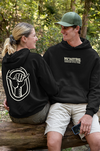 Two people wearing black hoodies with visible Mo' Bettahs branding, sitting on a log outdoors.