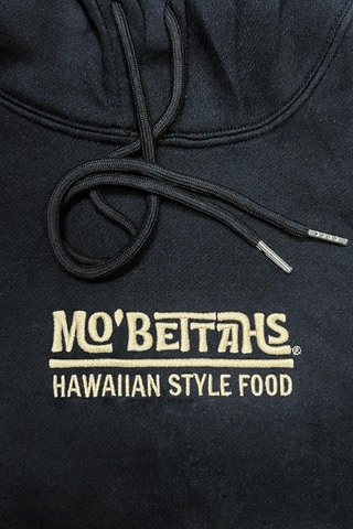 Black hoodie with 'Mo' Bettahs Hawaiian Style Food' text in sand color on a close-up view.