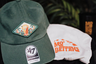 The green Mo' Bettahs Patch hat with graphic and white t-shirt with Mo' Bettahs island logo in orange.