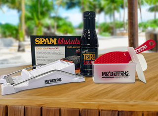 Mo' Bettahs Spam Musubi Making Kit .Shows Spam Slicer, a bottle of Mo' Betthas Teri Sauce, a red rice paddle, a Spam Musubi press and a recipe card. 