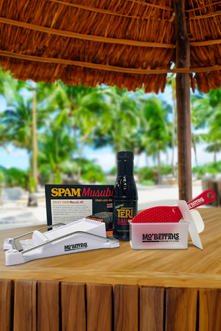 Mo' Bettahs Spam Musubi Making Kit. Shows Spam Slicer, a bottle of Mo' Betthas Teri Sauce, a red rice paddle, a Spam Musubi press and a recipe card. 
