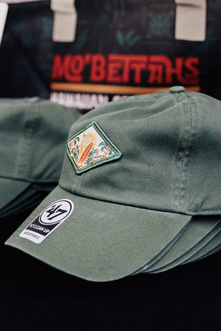 Several Mo' Bettahs Patch Hats in a stack with Mo' Bettahs Tote in background.