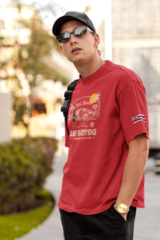 Man in city wearing Mo' Bettahs Teri Sauce red T-shirt, showing front Teri Sauce graphic and Hawaiian flag graphic on left sleeve.