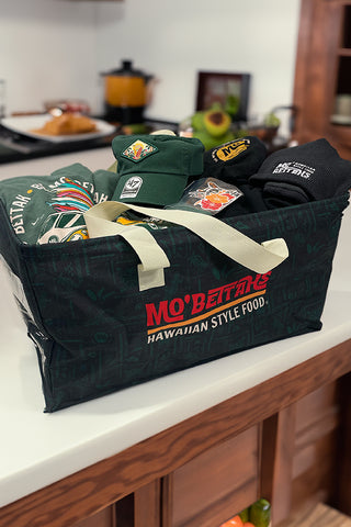 Mo' Bettahs Utility Tote sitting on countertop in kitchen, filled with Mo' Bettahs swag: T-shirts, hats, stickers, etc.